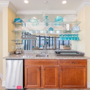 Wet bar area featuring a sleek granite countertop, stainless appliances, and decorative glassware