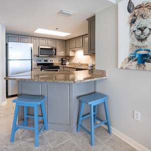 Modern kitchen features granite countertops, blue bar stools, and a whimsical llama artwork, creating a fun cooking space