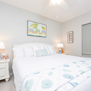 Guest bedroom featuring a king bed with soft linens, decorative shell-patterned throw, and beach-themed artwork