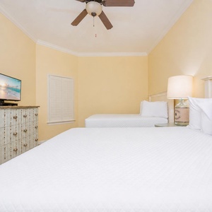 Relaxing guest bedroom featuring two cozy queen beds, a TV, and charming decor against a soft yellow backdrop