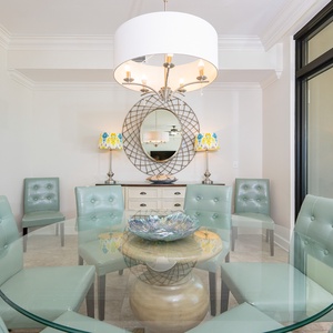 Elegant dining area featuring a glass table, mint green chairs, and a beautiful view of the beach from the balcony
