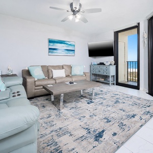 Cozy living area features a light blue sofa, decorative pillows, and a view of the beach through large sliding glass doors