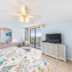 The master bedroom features a king bed, a TV, and a cozy sitting area with access to a balcony