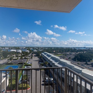 Master balcony view showcasing the vibrant blue tennis courts and lush greenery, with a view of the surrounding community