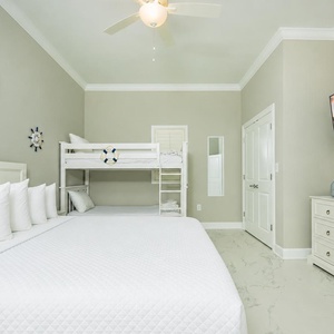 Experience comfort in this inviting guest bedroom featuring a king bed, twin bunk beds, and a large TV