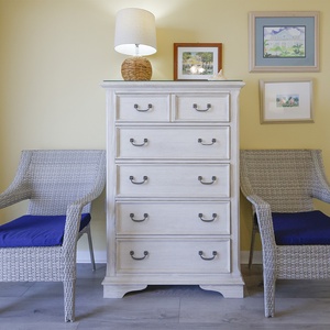Cozy corner features two wicker chairs with blue cushions flanking a light wood dresser in the master suite