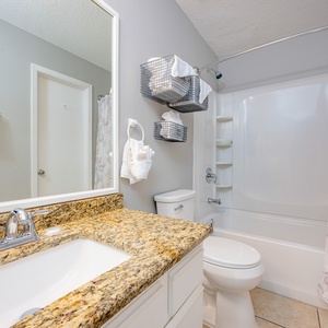 The bathroom features a granite countertop, decorative shower curtain, and a view into a softly lit bedroom