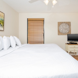 Spacious guest bedroom features a large king bed adorned with fluffy pillows, a flat-screen TV, and a serene beach painting