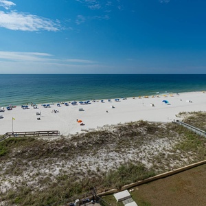 The view showcases a pristine beach with vibrant umbrellas and white sand, inviting relaxation under a clear blue sky