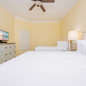 Relaxing guest bedroom featuring two cozy queen beds, a TV, and charming decor against a soft yellow backdrop