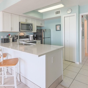 The kitchen features stainless steel appliances, a bright white countertop, and a breakfast bar, perfect for morning meals