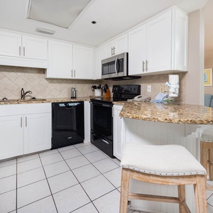 White cabinetry complements the granite countertops in this fully-equipped kitchen with a breakfast bar and seating