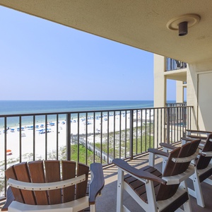 Balcony view overlooking a pristine beach with white sand and blue umbrellas lining the shore