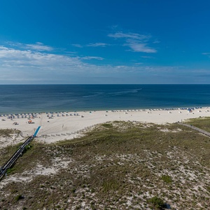 Expansive view of the beach with white sand, colorful umbrellas, and calm gulf waters under a clear blue sky