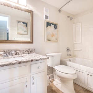 This bathroom features a stylish granite countertop, a large mirror, and a relaxing bathtub for a refreshing experience