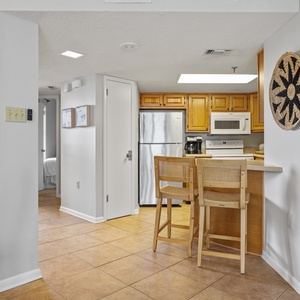 The kitchen features wooden cabinetry, a breakfast bar with seating, and a view into a cozy guest bedroom area