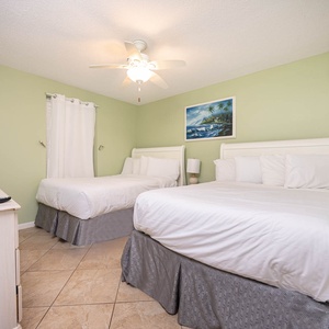 This guest bedroom features two comfortable double beds, a flat-screen TV, and soothing green walls accented by beach art