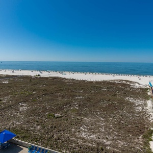 Expansive view of the beach with white sand and umbrellas, accessible via a wooden walkway from the propertyâ€™s pool area