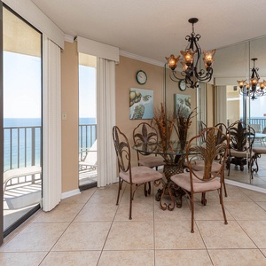 Dining area features a glass table with by elegant wrought iron chairs, with a stunning beachfront view through large windows