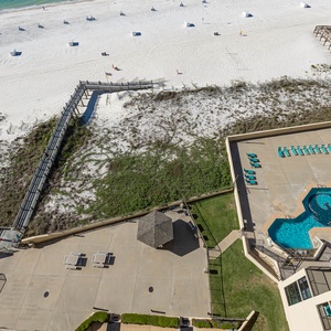 Balcony view showcasing the pool area with turquoise loungers, a shaded gazebo, and a pathway leading to the beach front