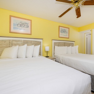 Bright yellow walls complement two double beds with white linens and decorative pillows, creating a cheerful guest room
