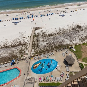 The view showcases the vibrant pool area with a pirate ship splash park, surrounded by sun loungers and the beach