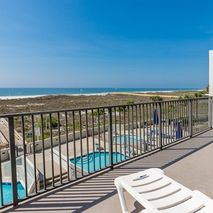 Outdoor balcony view showcasing the pool area and the beach, with a wooden walkway leading to the gulf in the distance