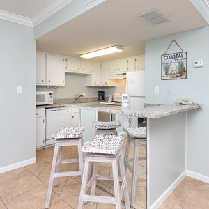 The kitchen features light cabinetry, a breakfast bar, and a cozy coastal decor, perfect for meal prep and gatherings