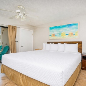 Efficiency-style bedroom featuring a plush king bed and vibrant beach-themed artwork, with access to a private balcony