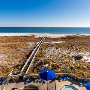 Impressive view of the beach with white sand, a boardwalk leading to the shore, and a pool area with blue umbrellas below