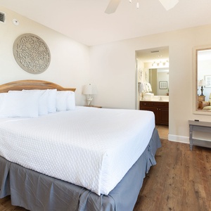 Spacious master suite features a plush king bed, a wooden dresser, and a mirror reflecting the adjoining bathroom