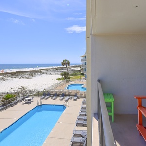 Enjoy a vibrant view from the balcony overlooking the pool and beach, with colorful chairs inviting relaxation