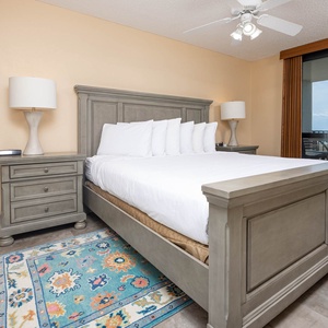 Master bedroom features a king bed with plush pillows, a stylish nightstand, and access to a balcony with gulf views