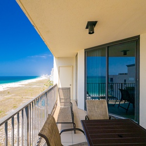 Spacious balcony with a table and chairs offers a serene view of the beach and sparkling gulf waters
