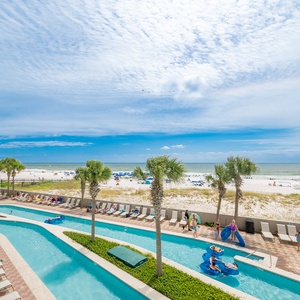 Bask in the sun by the lazy river with a stunning view of the beach and vibrant umbrellas in the distance