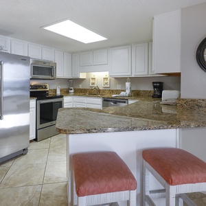 Bright kitchen area features granite countertops, modern appliances, and a breakfast bar with coral-colored stools