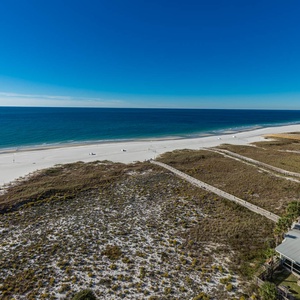 Expansive view of the tranquil gulf and white sand beach, framed by lush dunes and a nearby pool area