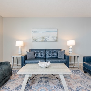 The living area features plush seating, a decorative coffee table, and coastal artwork, creating a relaxed atmosphere