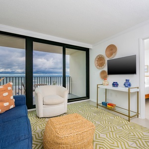 The inviting living area features a cozy blue sofa, a flat-screen TV, and stunning beachfront views through large glass doors