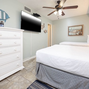 The guest bedroom features two comfortable beds, a large TV, and charming coastal decor for a relaxing stay