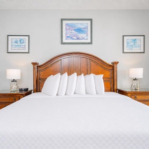 A wooden headboard frames a plush king bed in the master, with bedside lamps and coastal artwork, creating a serene retreat