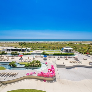 Enjoy a vibrant pool area with lounge chairs and colorful floats, set against a picturesque coastal landscape