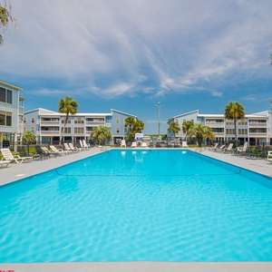 Dip into the shimmering pool surrounded by palm trees and charming blue buildings, perfect for your getaway to Sea Oats
