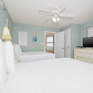 Bright guest bedroom featuring two double beds, a dresser with a TV, and coastal decor, creating a relaxed atmosphere