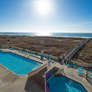 Pool area with turquoise loungers, leading to a scenic boardwalk that connects to the beach and sparkling gulf waters
