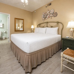 Cozy guest bedroom featuring a large king bed with soft linens, a decorative seashell wall piece, and a charming nightstand