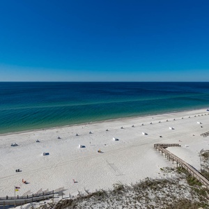 A panoramic view showcases a pristine beach with white sand, dotted with lounge chairs under a clear blue sky
