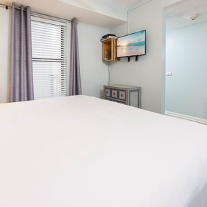 Master suite featuring a king bed, a mounted TV, and soft natural light from the window with elegant curtains