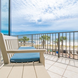 Relax on the balcony with comfortable seating and enjoy the serene view of the pristine beach, pool area, and palm trees