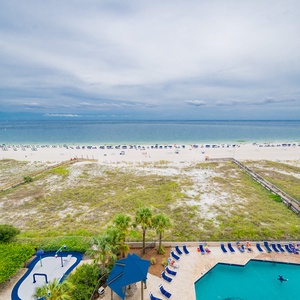 Enjoy the inviting pool area surrounded by lounge chairs and lush greenery, with the beach just a short stroll away